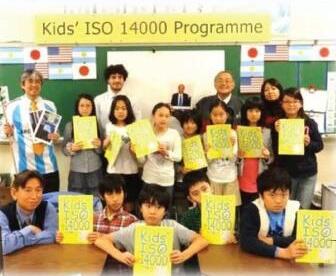 「Kids’ ISO 14000 Programme」の横断幕の前で、黄色い冊子を手にした子どもたちと先生たち
