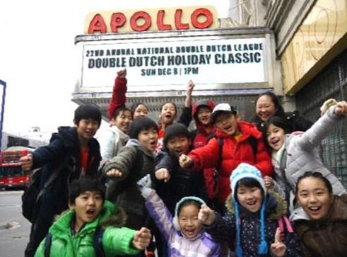 「DOUBLE DUTCH HOLIDAY CLASSIC」の看板がかかったアポロシアターの前で、ポーズをとる子どもたち