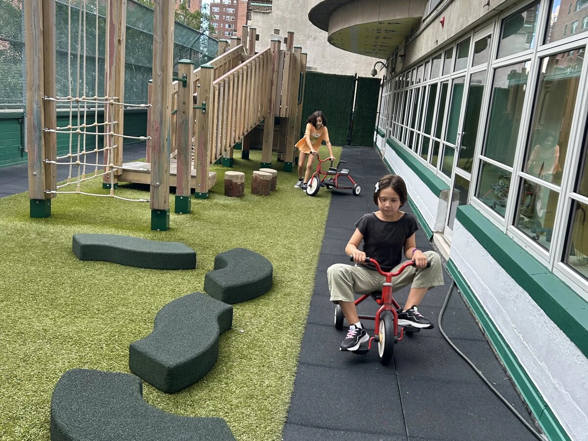 専用の屋外プレイエリアで三輪車に乗る子ども