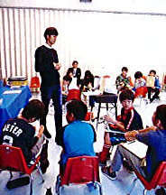 教室で子どもたちに語りかける大学生と、席に着いた子どもたち