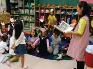 床に座った幼児たちに先生が絵本を読み聞かせる教室