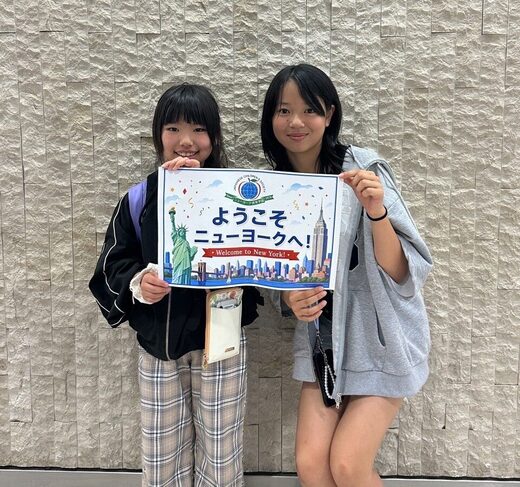 「ようこそニューヨークへ！」のボードを持つ植杉紗依さんと橋本千穂さん