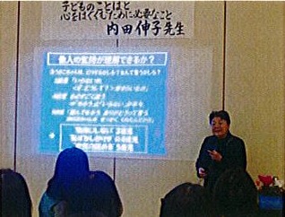 スクリーンの横に立って講演する内田伸子先生と、聞き入る参加者